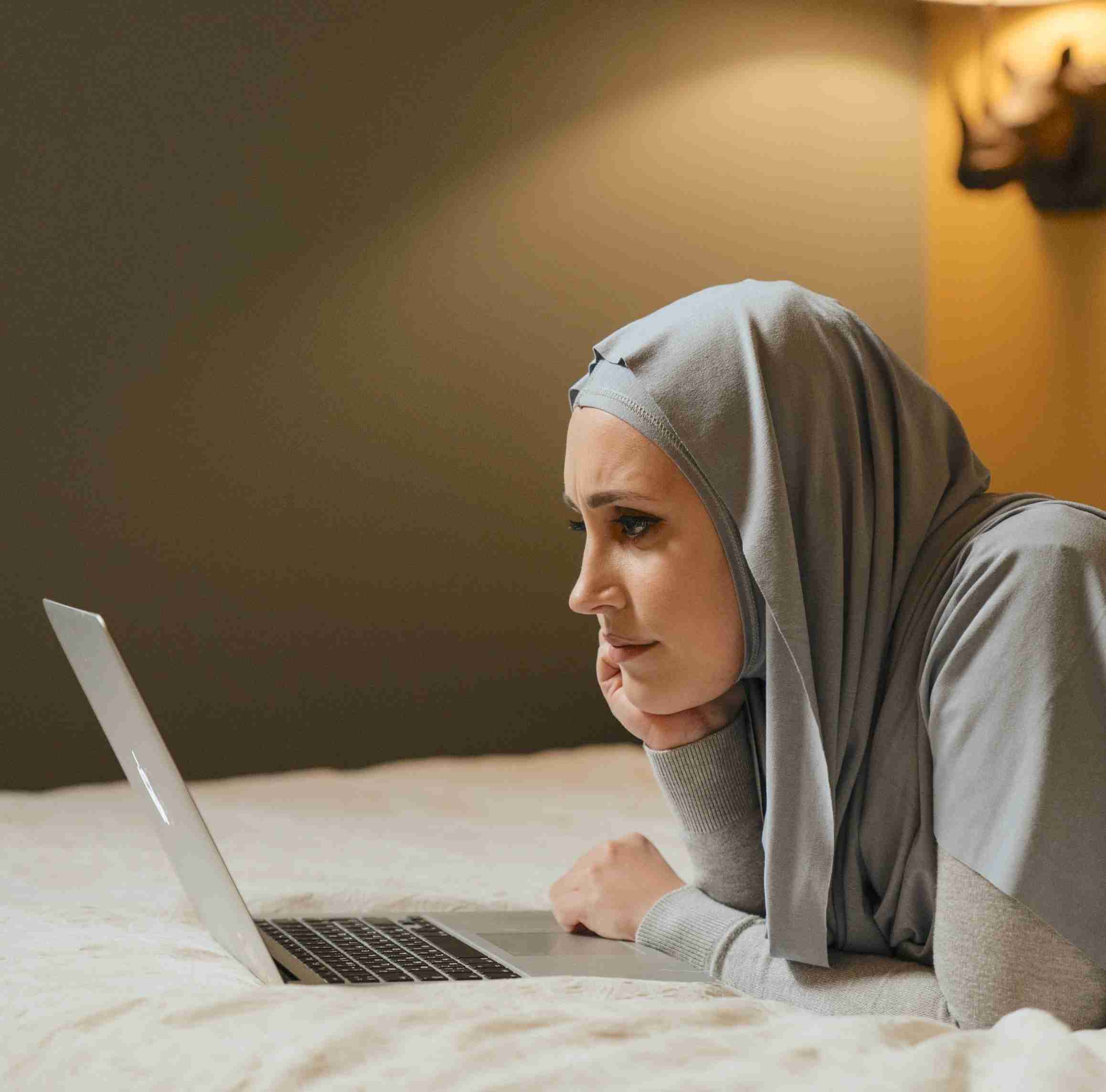 Woman laying in bed looking at laptop in tele therapy session.