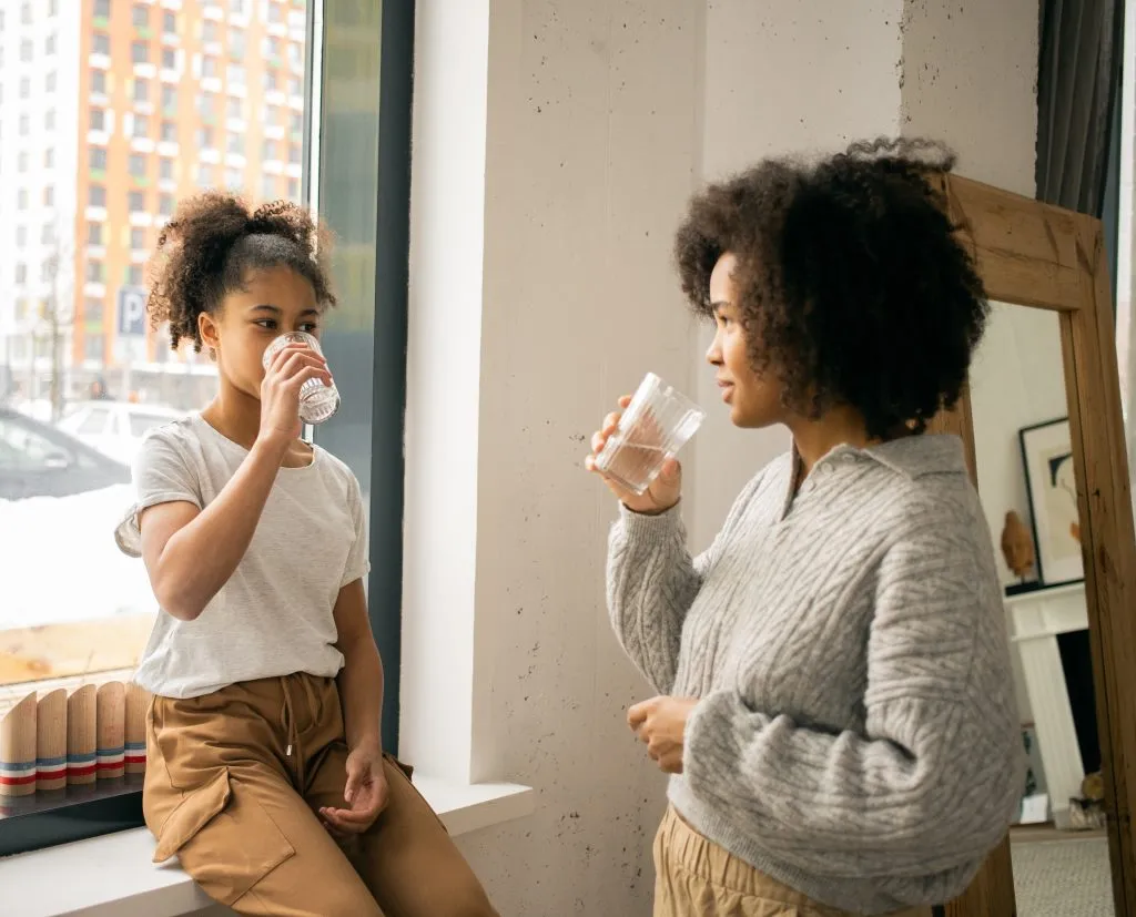 A black mother and daughter sip water together, illustrating that Susan Gonzales helps parents and children.