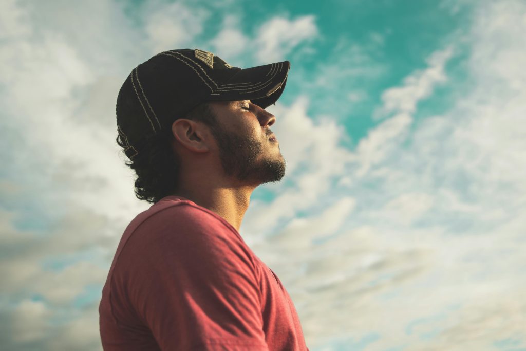 man with a red shirt and baseball cap seemingly taking a deep breath outside